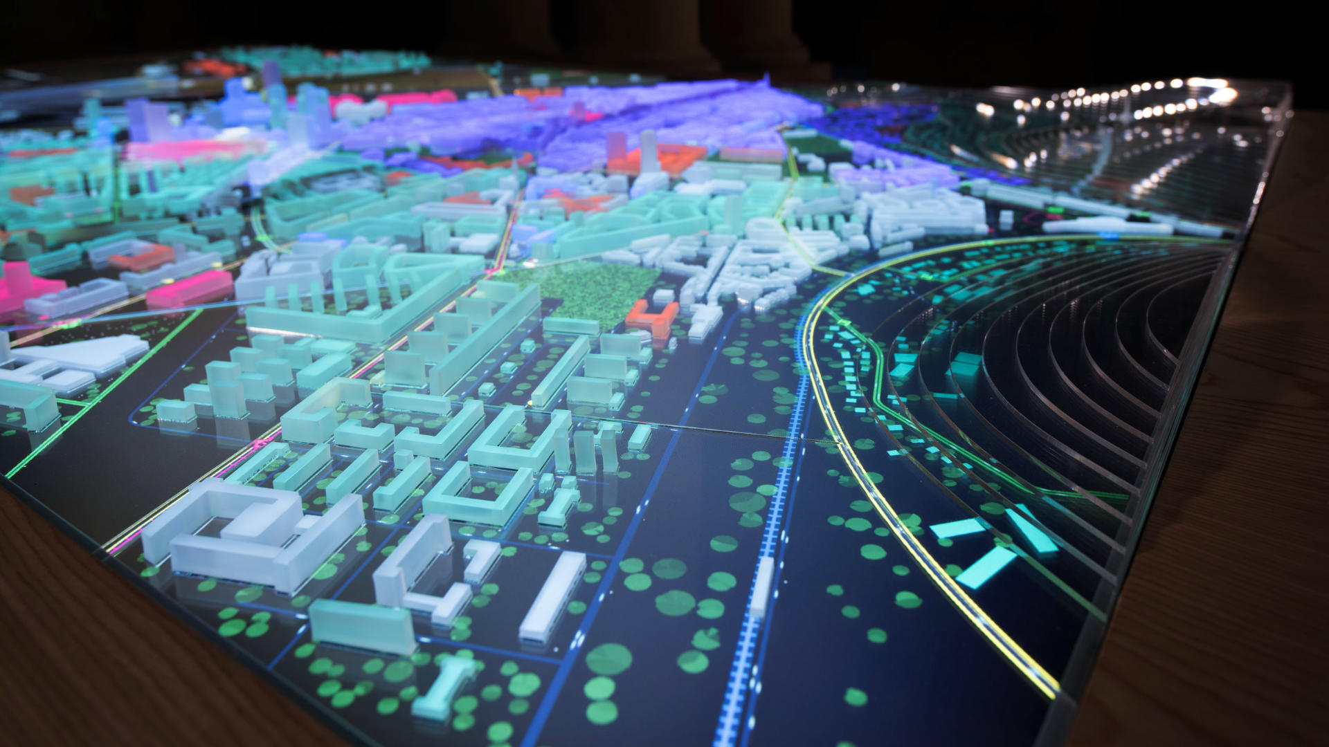 a photo of the lit up physical city model with multiple plastic urban elements highlighted in green, orange and purple