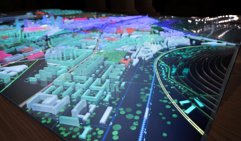 a photo of the lit up physical city model with multiple plastic urban elements highlighted in green, orange and purple